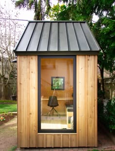 a small wooden building with a black roof and glass doors on the outside, sitting in front of a tree