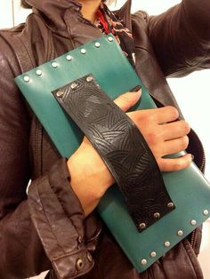 a woman is holding a green and black leather case with rivets on it