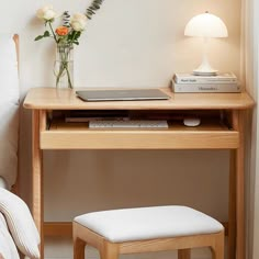 a wooden desk with a laptop and flowers on it next to a bed in a bedroom