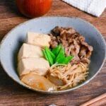 a bowl filled with meat and vegetables next to an apple