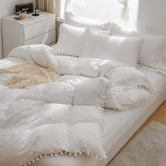 an unmade bed with white comforters and pillows on top of it in front of a window