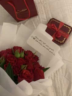 a bouquet of red roses sitting on top of a bed next to a card box