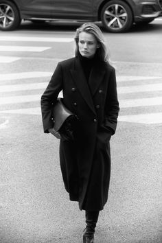 black and white photograph of woman in coat crossing street