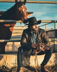 a man wearing a cowboy hat sitting in front of a fence next to a horse