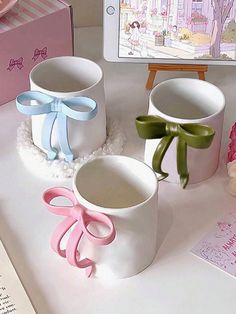 two white cups with bows on them sitting next to a pink box and an ipad