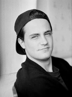 a black and white photo of a young man wearing a baseball cap, looking at the camera