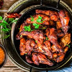 chicken wings in a frying pan with garnishes on the side