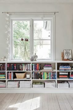 a white book shelf filled with lots of books next to a window in a room