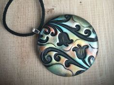 a round pendant with black and silver designs hanging from a cord on a wooden surface