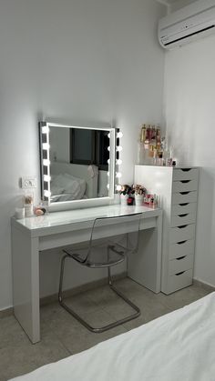 a white desk with a mirror and lights on it in front of a bed,