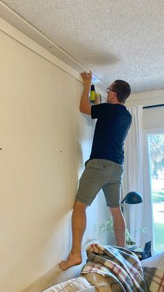 a man is painting the wall in his bedroom with white paint and wood planks