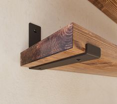 a wooden shelf mounted to the side of a wall next to a metal hook on a white wall