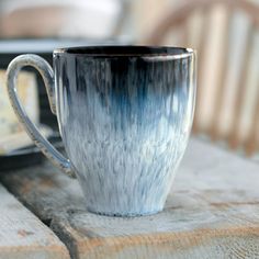 a blue and white coffee cup sitting on top of a wooden table next to a plate