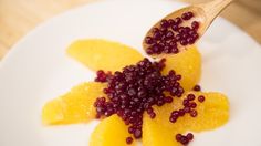 a white plate topped with orange slices and pomegranates next to a wooden spoon