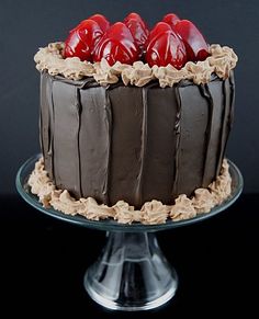 a cake with chocolate frosting and red cherries on top sitting on a plate