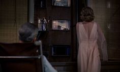 a woman in a pink dress standing next to a man in a chair looking out the window