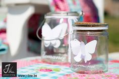 two glass jars sitting on top of a table covered in paper butterfly cutouts