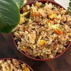 two bowls filled with rice and vegetables on a wooden table next to a green leaf