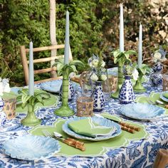 the table is set with blue and green plates, napkins, candles and vases