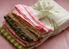 a stack of folded cloths sitting on top of a pink tablecloth covered in green and white designs