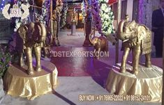 two gold elephants on pedestals in front of an entrance to a building decorated with flowers and greenery