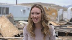 a young woman standing in front of a pile of wood and rubble with her eyes closed