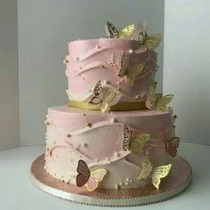 a three tiered cake with pink frosting and gold butterflies