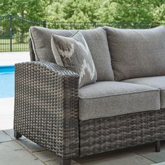 a couch sitting on top of a patio next to a swimming pool with trees in the background