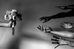 black and white photograph of brides hands reaching out to each other with their wedding bouquet