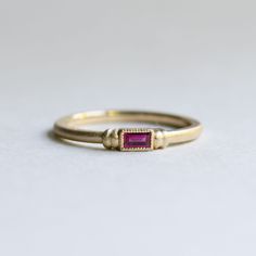 a yellow gold ring with a pink tourmaline stone set in the center, on a white background