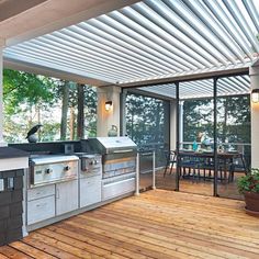 an outdoor kitchen and dining area on a deck with wood flooring, covered by a pergolated roof