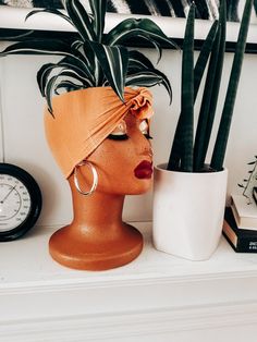 a woman's head wearing an orange turban next to a potted plant