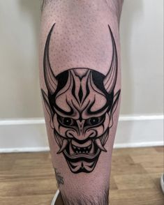 a man's leg with a black and white tattoo design on it, depicting a demon