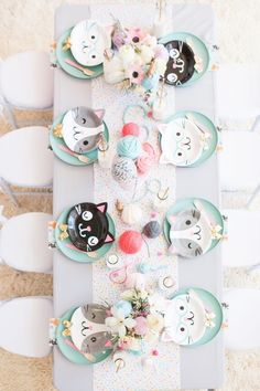 an overhead view of a table with plates and cupcakes on it, decorated with cats