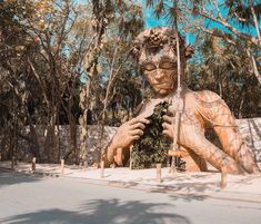 a large wooden statue sitting on the side of a road in front of some trees