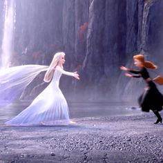 two women dressed as disney characters dancing in front of a waterfall with their arms outstretched