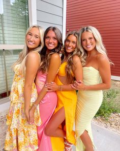 four beautiful young women standing next to each other in front of a red house and smiling at the camera