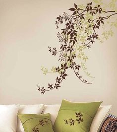 a living room with a white couch and green pillows on top of the sofa is decorated with an artistic wall decal