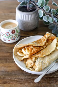 some pancakes on a white plate next to a cup of coffee and a potted plant