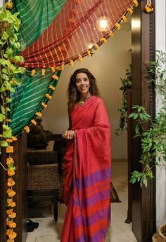 a woman in a red and purple sari standing at the entrance to her home