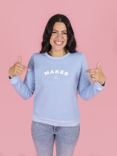 a woman wearing a blue sweater with the word maker written on it and two fingers up