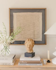 a table topped with books and a vase filled with flowers next to a busturine