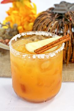 a drink with an apple and cinnamon garnish on the rim next to a decorative pumpkin