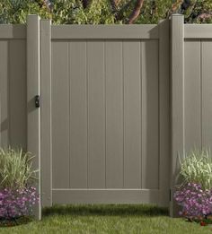 a gray fence with purple flowers in the grass