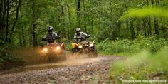 two people riding on four wheelers through the woods