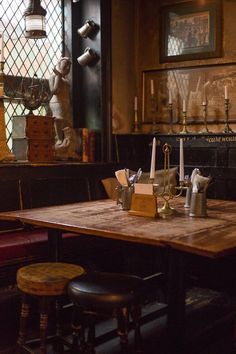 a wooden table topped with lots of bottles and glasses next to two stools in front of a stained glass window