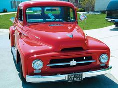 an old red truck is parked on the side of the road in front of a house