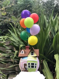 a small house with balloons attached to it's roof in front of some plants