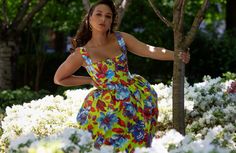 a woman in a colorful dress leaning against a tree