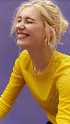 a woman smiling while holding a tennis racquet in her hand and wearing a yellow shirt